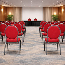 Konferenčná stolička s červeným čalúnením a čiernym rámom.